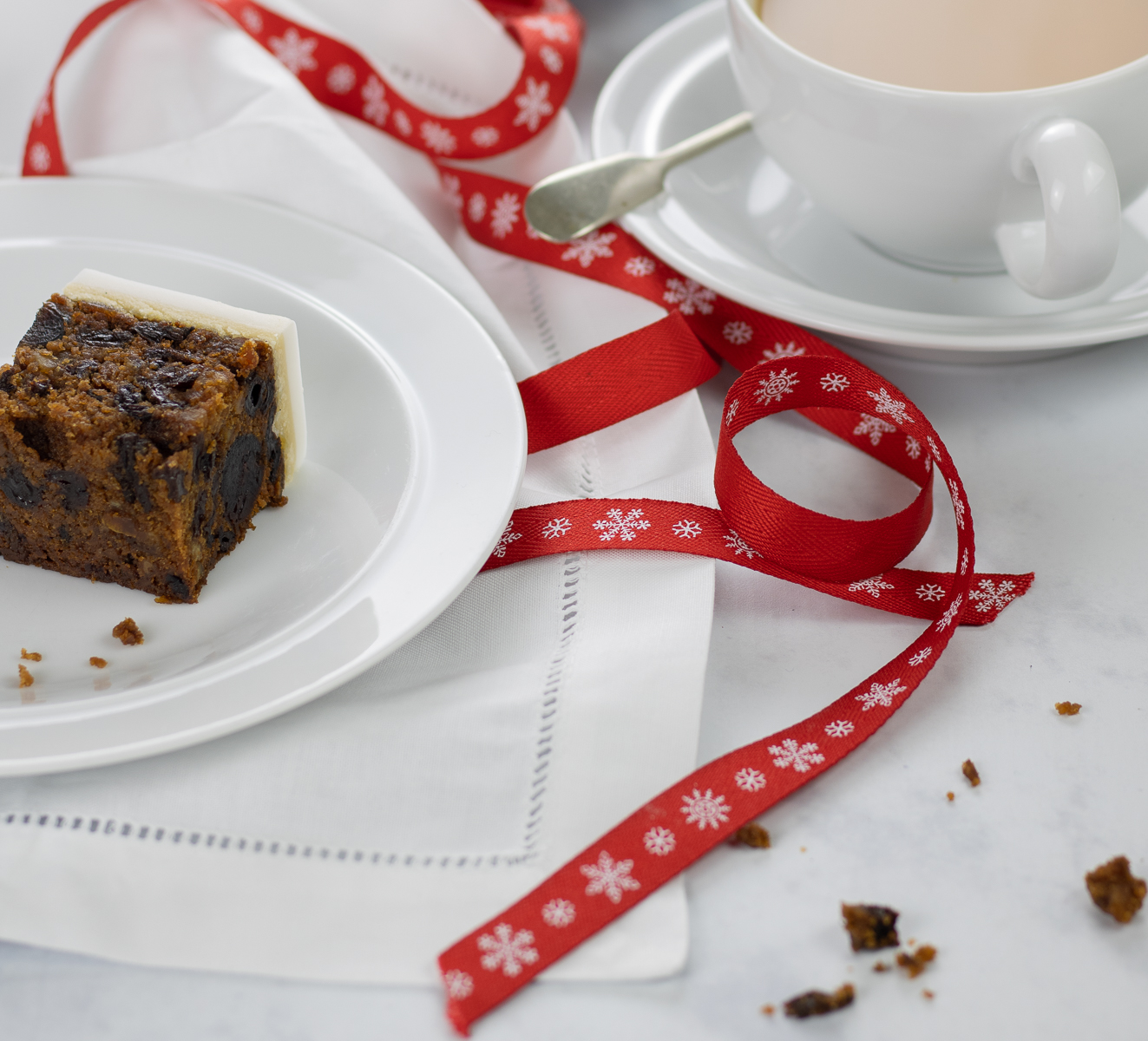 Xmas cake with red ribbon on plate with crumbs and tea